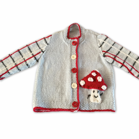 Knitted children's cardigan with red trim and mushroom design on a white background, Fun guy Mushroom cardigan knitted pattern for babies with plaid sleeves. jane burns designs
