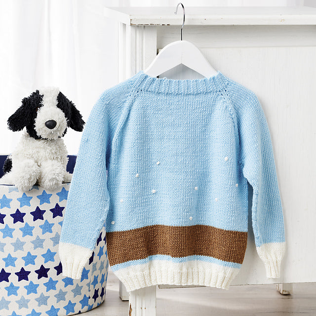 Dachshund in the snow, a kids cardigan knitting pattern with a wrap around intarsia sausage dog with knitted applique elements to bring it to life. Seamless top down cardigan knitting pattern for children by jane burns