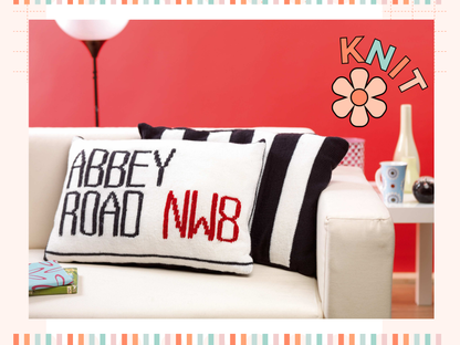 Image shows two knitted cushions one showing the abbey road street sign and behind it a second black and white striped cushion looking like the zebra crossing from the beatles music album knitting pattern by jane burns