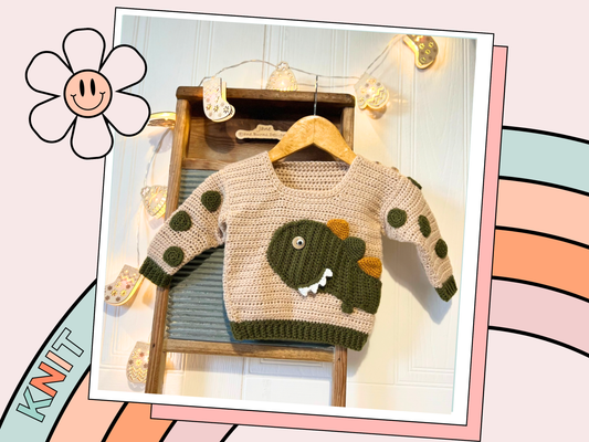 beige crochet sweater with moss green cuff, featuring a moss green dinosaur applique, mustard and moss green spikes run down the spine of the dinosaur. the dinosaur has white teeth and googly eye. the sleeves of the jumper has crochet spots sewn to them. dinotastic crochet sweater pattern for babies and toddlers by jane burns