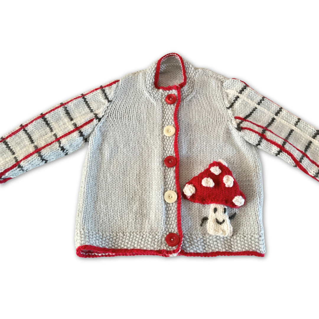 Knitted children's cardigan with red trim and mushroom design on a white background, Fun guy Mushroom cardigan knitted pattern for babies with plaid sleeves. jane burns designs