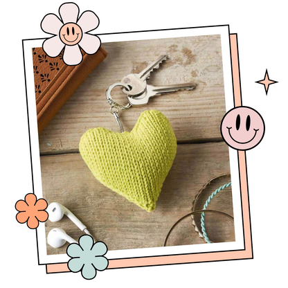 Yellow knitted heart keychain on a wooden surface with decorative elements. Valentines knitted heart keyring pattern jane burns