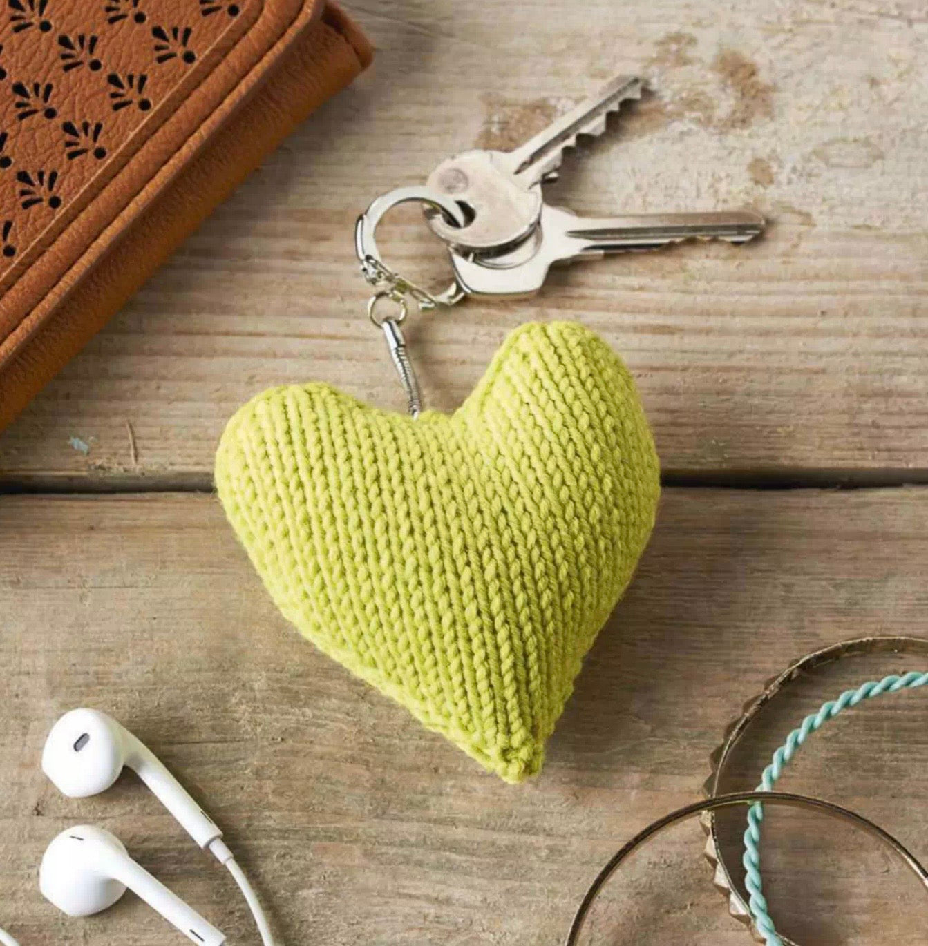 Yellow knitted heart keychain on a wooden surface with decorative elements. Valentines knitted heart keyring pattern jane burns