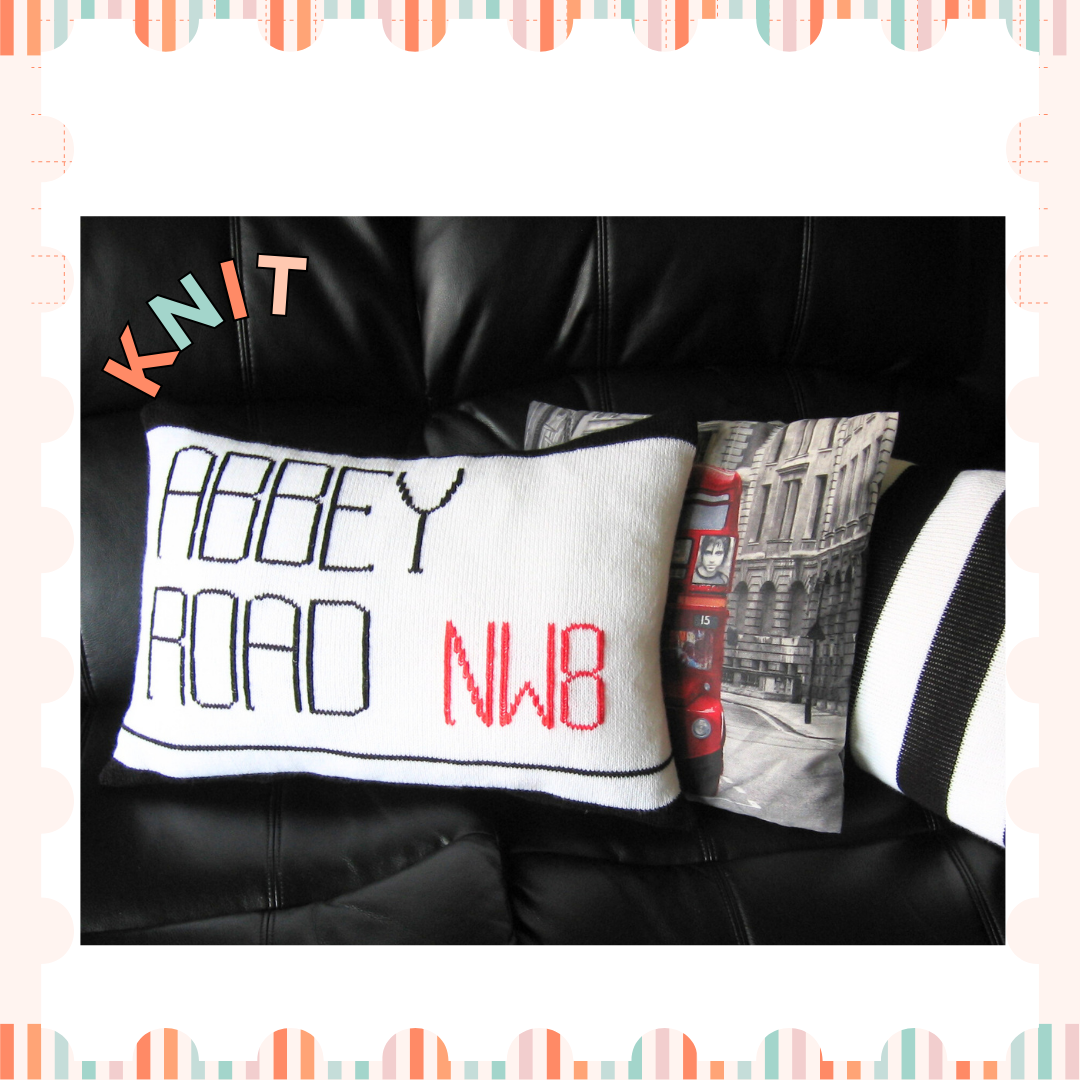 Image shows two knitted cushions one showing the abbey road street sign and behind it a second black and white striped cushion looking like the zebra crossing from the beatles music album knitting pattern by jane burns