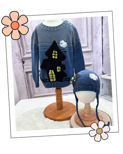 A blue knit sweater and matching blue knit hat displayed on mannequin stands in an indoor styled setting. The sweater features a large black house with yellow window details and a small white cloud motif. Halloween hats collection knitting patterns addition to the ghost house jumper shown