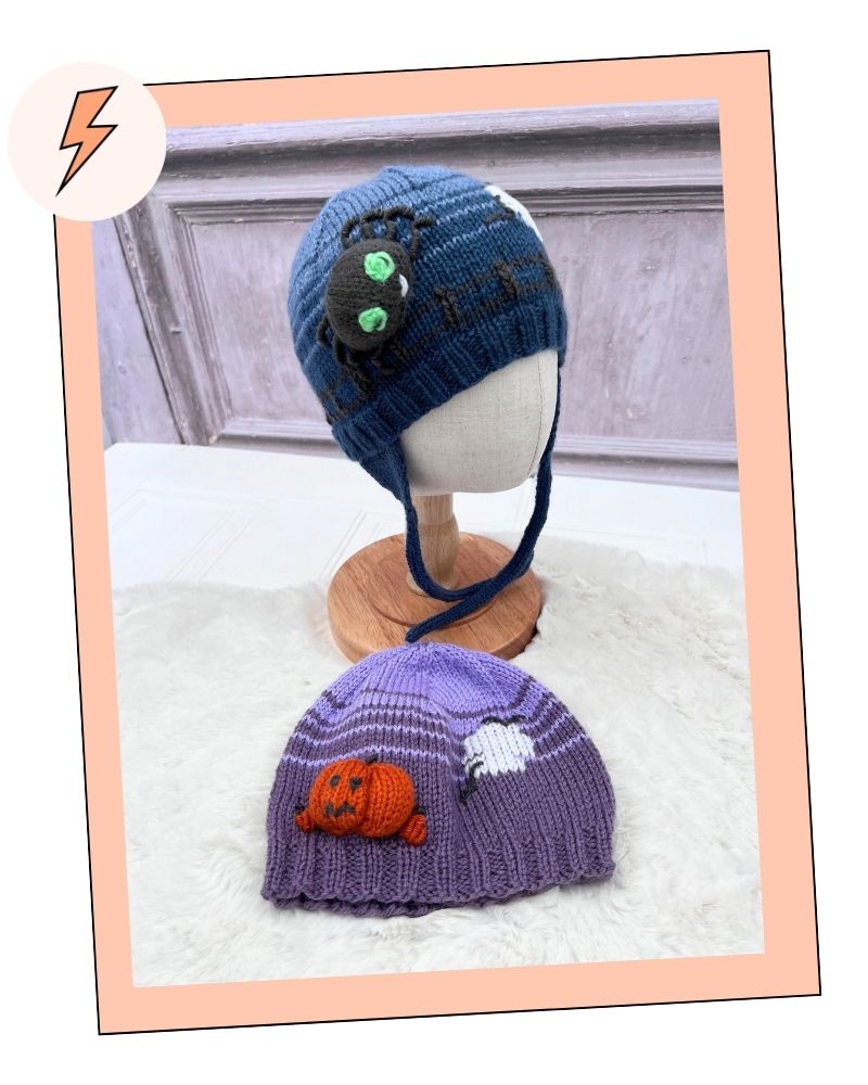 Halloween Hats, mix and match collection knitting patterns by Jane Burns. 
Two knitted baby hats displayed on a mannequin stand and a surface, with a peach border around the photo. The top hat is dark blue with a crocheted spider decoration and green eyes.