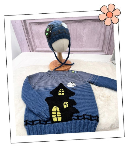 Mix and Match Halloween Hats Knitting Pattern Collection by Jane BurnsA blue knit children's sweater with a black haunted house and yellow windows, displayed on a white faux-fur surface with a matching blue knit hat on a mannequin head in the background.
