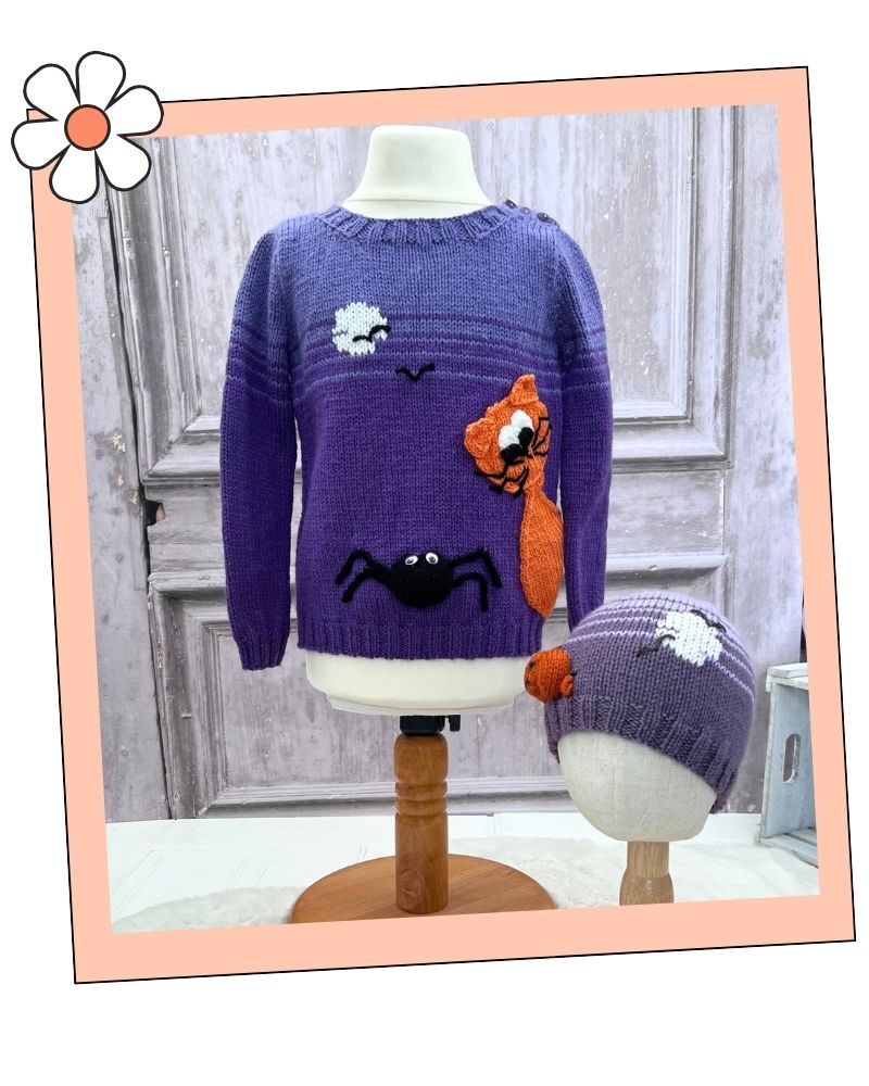 Mix and Match halloween hats knitting pattern collection by Jane Burns.
A purple knit sweater displayed on a mannequin stand, featuring a black spider, orange fox, white cloud, and black bird motifs. A matching purple knit beanie with a white cloud motif is shown on a smaller mannequin stand to the right.