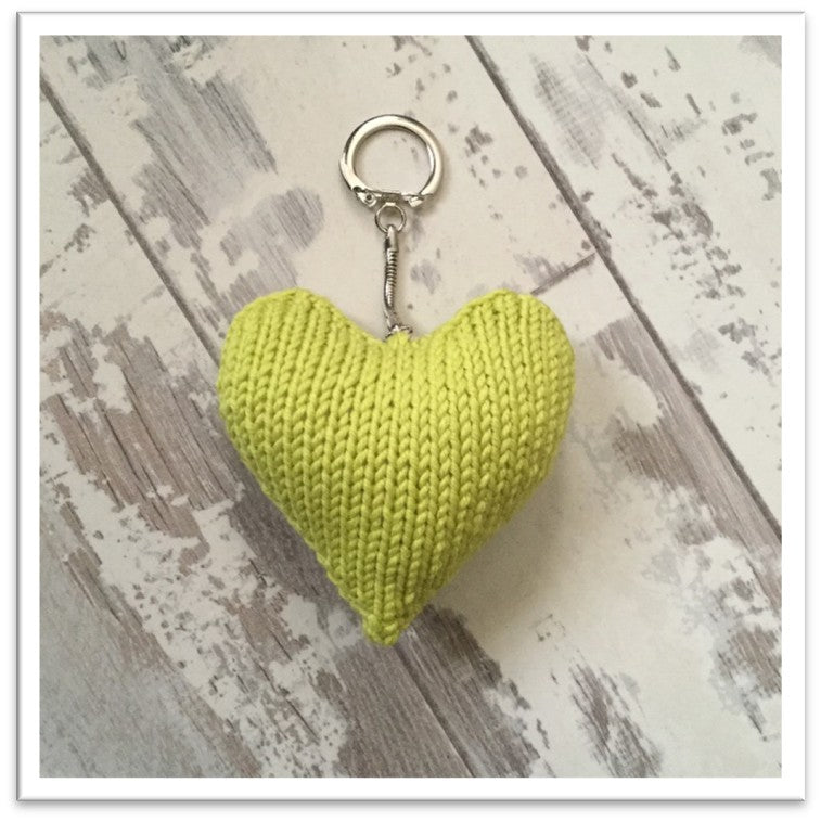 Yellow knitted heart keychain on a wooden surface with decorative elements. Valentines knitted heart keyring pattern jane burns
