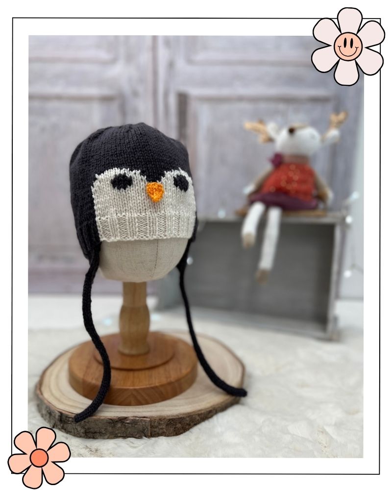 Penguin earflap hat with long i-cord ties on a wooden stand, baby and toddler hat knitting pattern