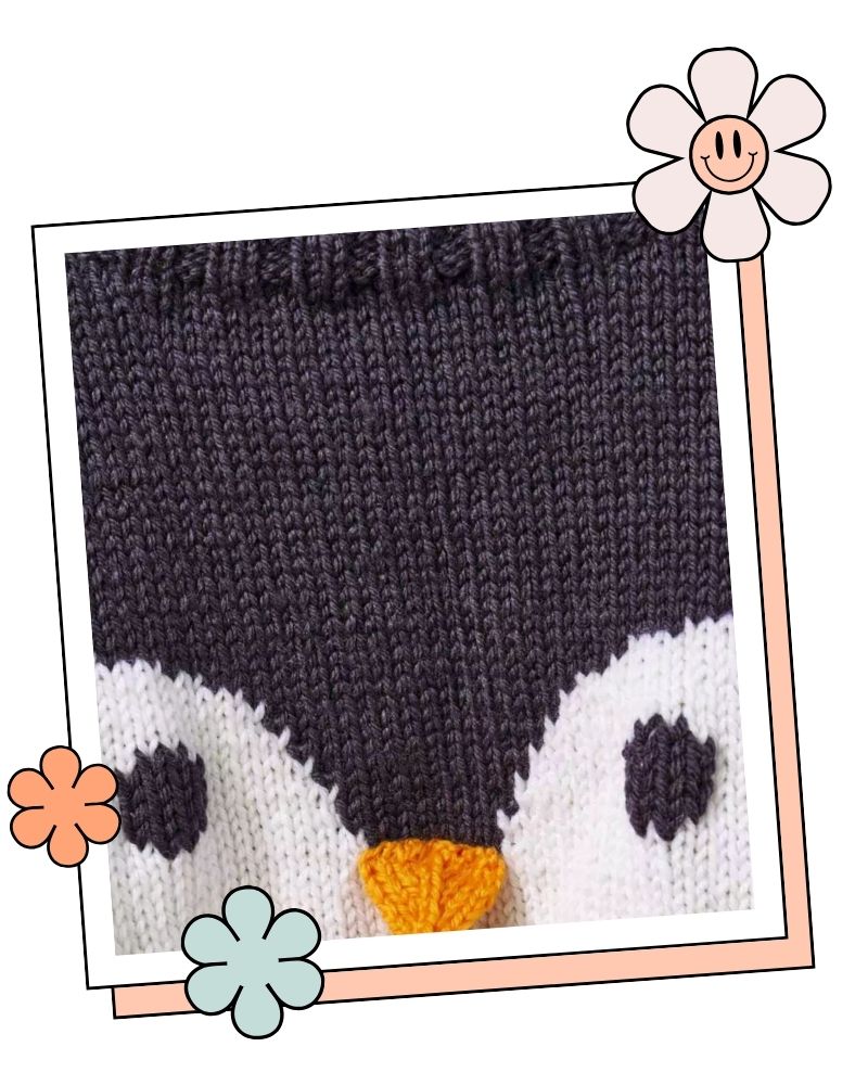 Close up of the knitted penguin face on the jumper, with black eyes and a 3D knitted orange beak