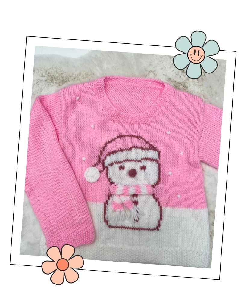 Close up of the snowman motif with sleepy eyes, a knitted 3D nose, pink and white stripy scarf with fringe and hat bobble