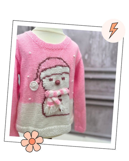Pink and white kids Christmas jumper laid flat, with French knot snowflakes and a white hem like fresh snow