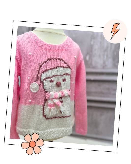 Pink and white kids Christmas jumper laid flat, with French knot snowflakes and a white hem like fresh snow