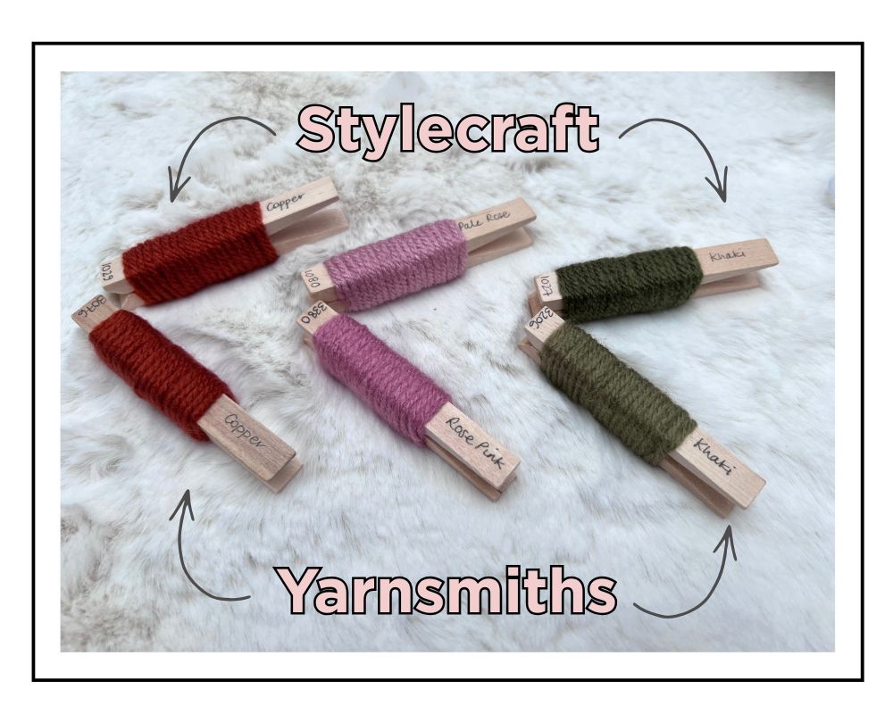 Five wooden clothespins holding wrapped yarn samples in red, pink, and olive green, arranged on a white faux-fur surface with decorative text reading 'Stylecraft' and 'Yarnsmiths'. Jane Burns Yarn Shade Comparison Guide PDF