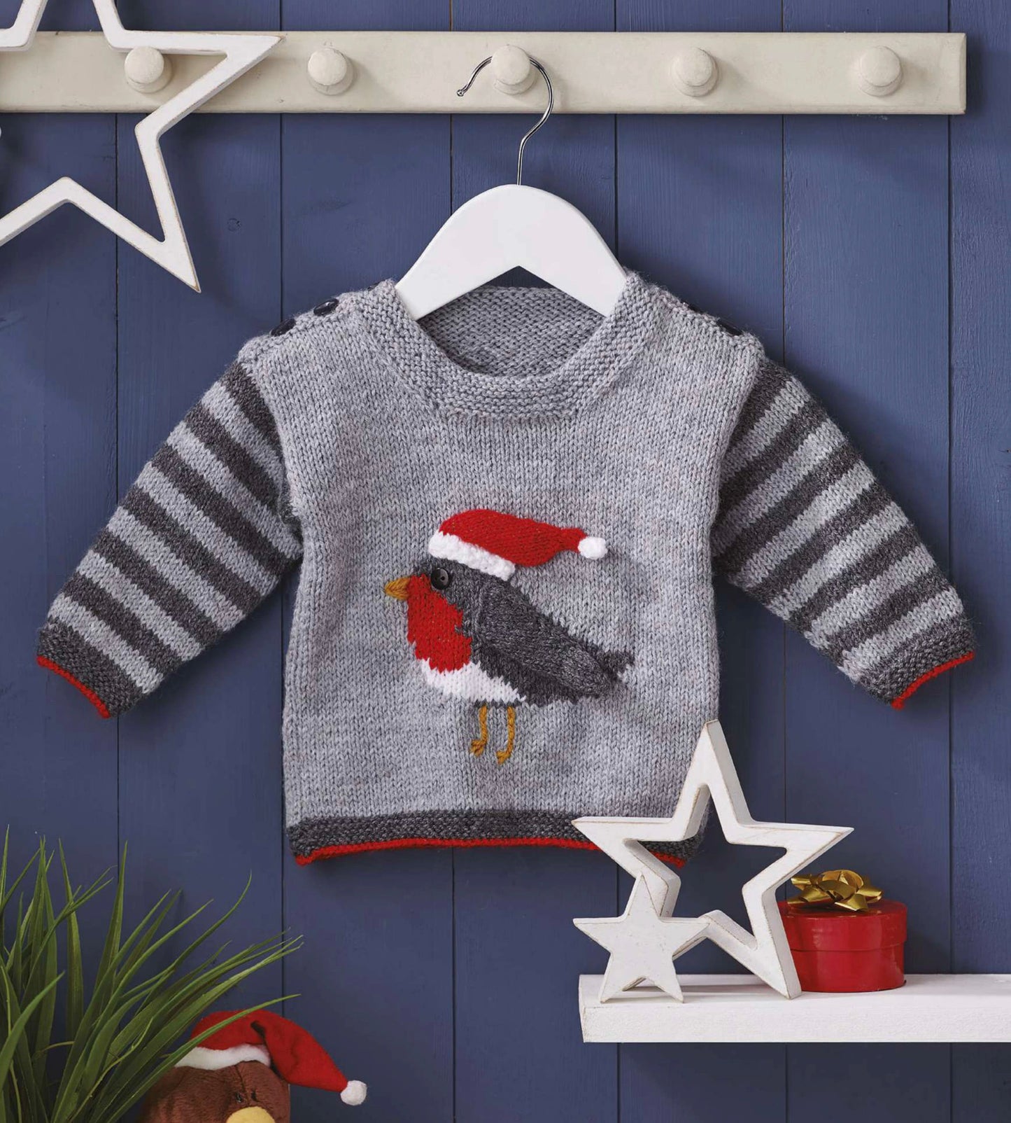 Rocking robin baby sweater, grey striped sleeves, with an intarsia robin on the front, the wing and hat are knitted and sewn on. The Hat can be removed after Christmas. DK yarn, designed by Jane Burns