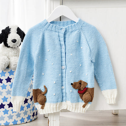 Dachshund in the snow, a kids cardigan knitting pattern with a wrap around intarsia sausage dog with knitted applique elements to bring it to life. Seamless top down cardigan knitting pattern for children by jane burns