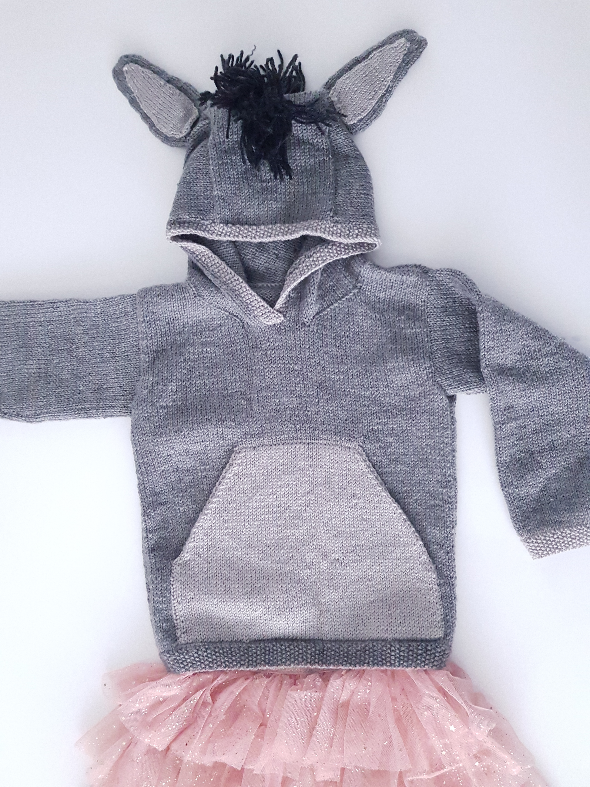 grey knitted hooded sweater with light grey kangaroo style pocket on the front, large donkey ears and a black mane create this cute donkey hoodie knitting pattern by jane burns